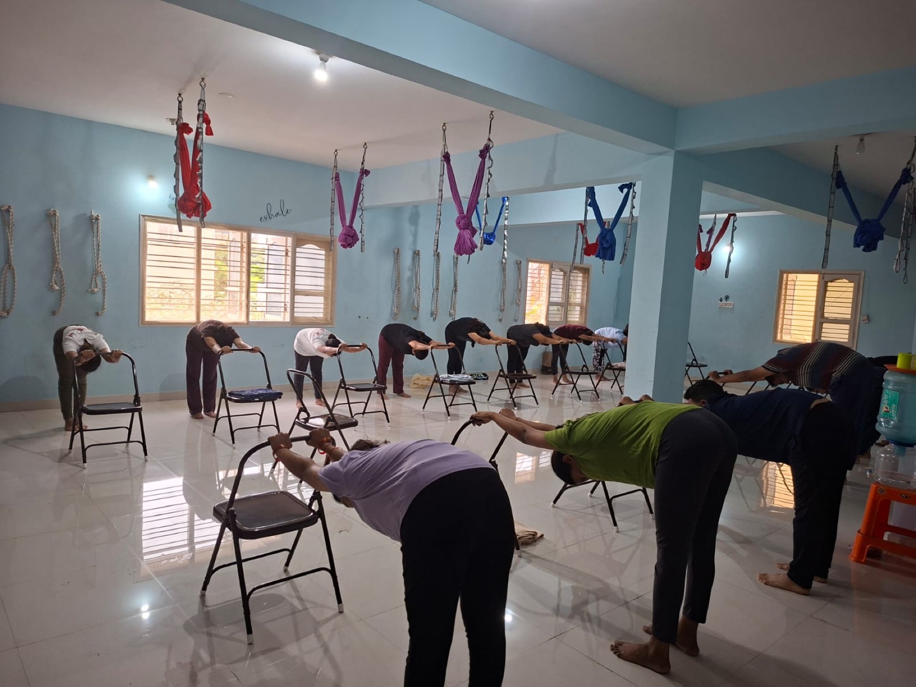 A full class folding forward over chairs at Astral Space Yoga, with aerial silks along the ceiling