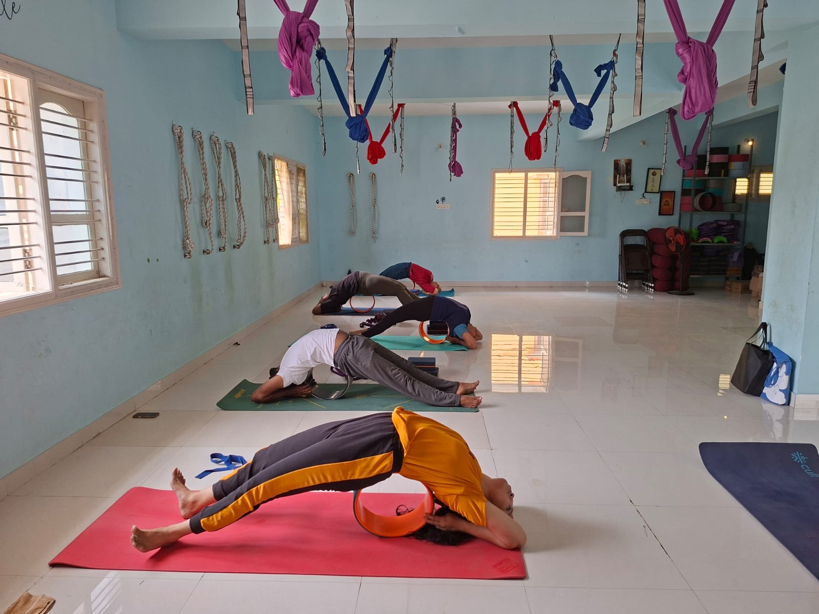 A small group using yoga wheels for a backbend on red and green mats